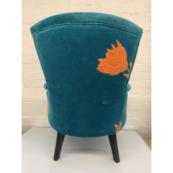 Image of the back view of a velvet turquoise arm chair with orange waratah embroidery.
