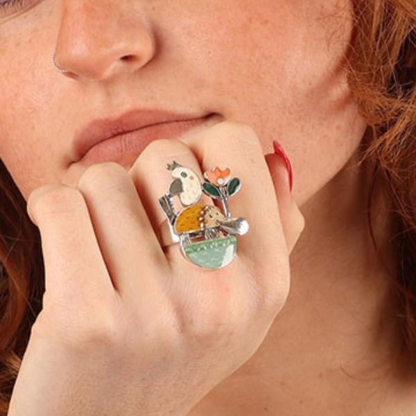Image of model wearing quirky ring featuring hand painted platypus, flowers and bird on silver metal finish.