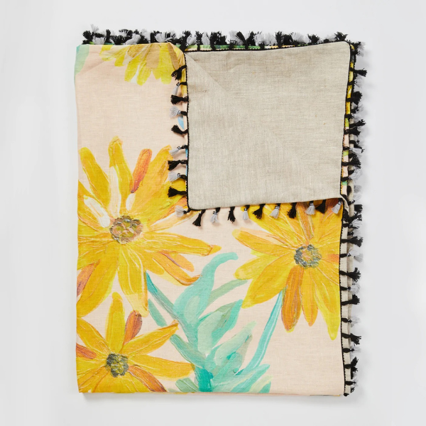 Image of linen throw with original dandelion print. Yellow flowers on peach background. Black and grey tassel edging.