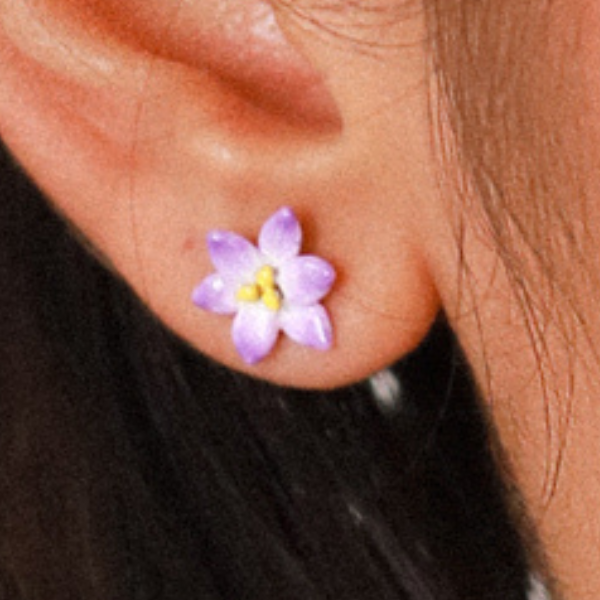 Image of model wearing tiny lilac flower earrings.