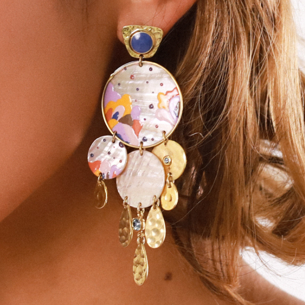 Image of model wearing statement creole style drop earrings with hand painted coloured patterns on a mop disc with multi gold dented teardrop dangles and crystalized stones below.