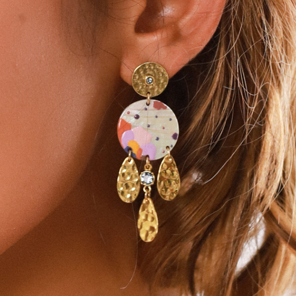 Image of model wearing gold plated stud earrings with a disc pink mop dangle hand painted in coloured patterns and 3 gold dangle teardrops with crystalized stone.