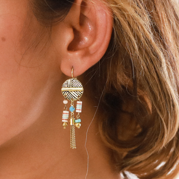 Image of model wearing ethnic style earrings with 3 dangle bone tubes on french hook gold plated finish.