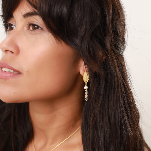 Image of model wearing single drop earrings comprising bone, speckled jasper and golden mother-of-pearl.