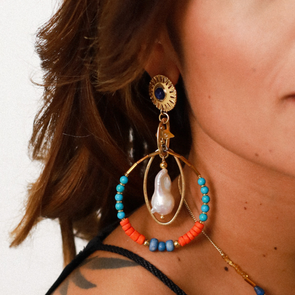 Image of round gold earring with blue stone centre and turquoise, orange and blue beads on a hoop dangle.