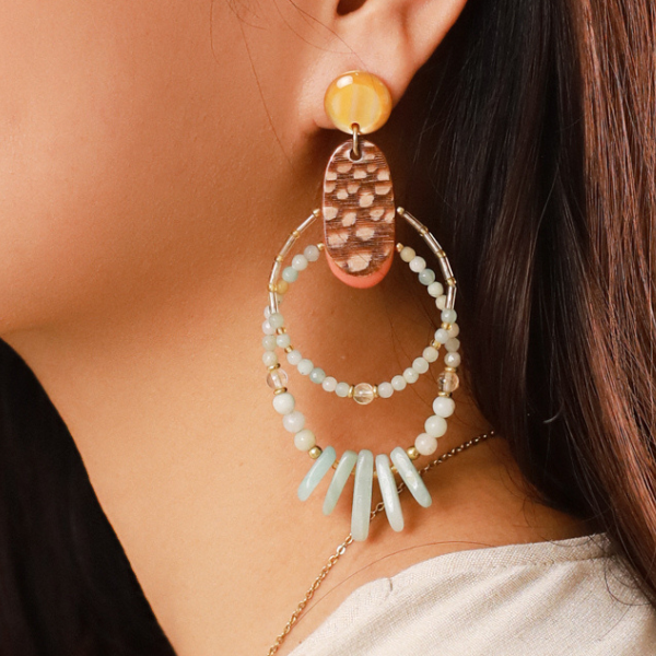 Image of model wearing stud earrings with two layer hoop dangles embellished in white and amber beads and semi precious stones.