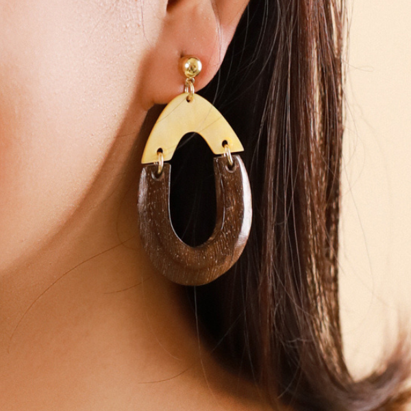 Image of model wearing big pear shaped earrings made from golden mother-of-pearl and robles on gold stud finish.