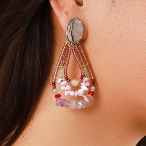 Image of model wearing 3 layer pear shaped drop earrings embellished in semi precious beads and stones in lilac tones with mint green and red featuring.