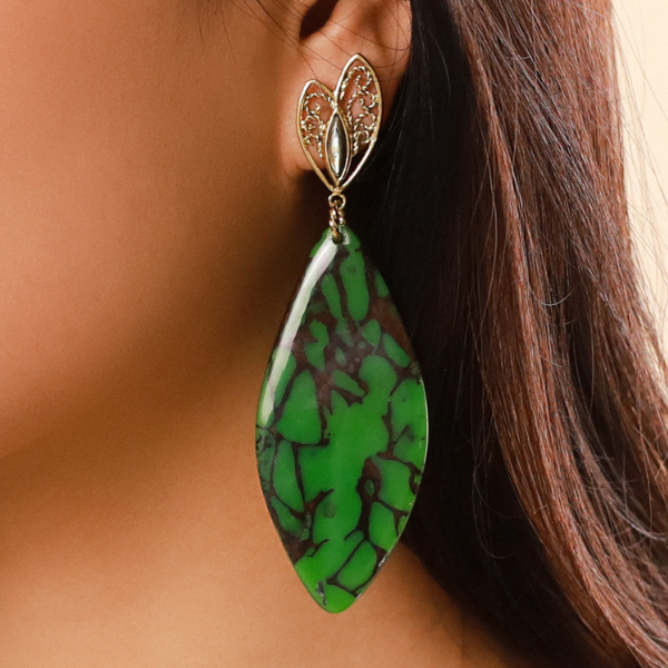 Image of model wearing large dangle earrings in termite mound malachite green colour and theme on gold plated stud finish.