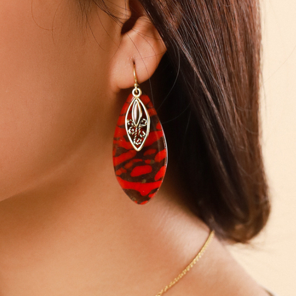 Image of model wearing dangle earrings in termite mound red agate colour and theme on gold plated hook finish.