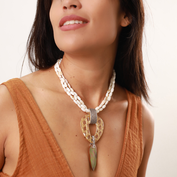 Image of model wearing a statement necklace with shell beads. Pendant consists of triangular, bamboo twine resin hoop trimmed with a teardrop shape brown lip piece.