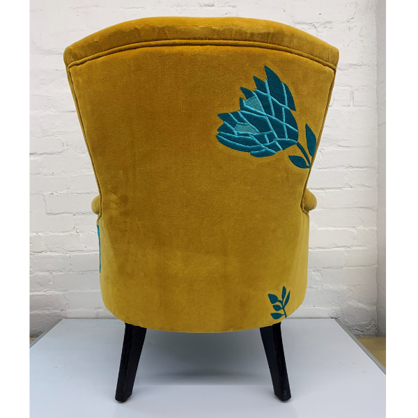 Image of back side of a velvet mustard arm chair embroidered with turquoise waratah embroidery.
