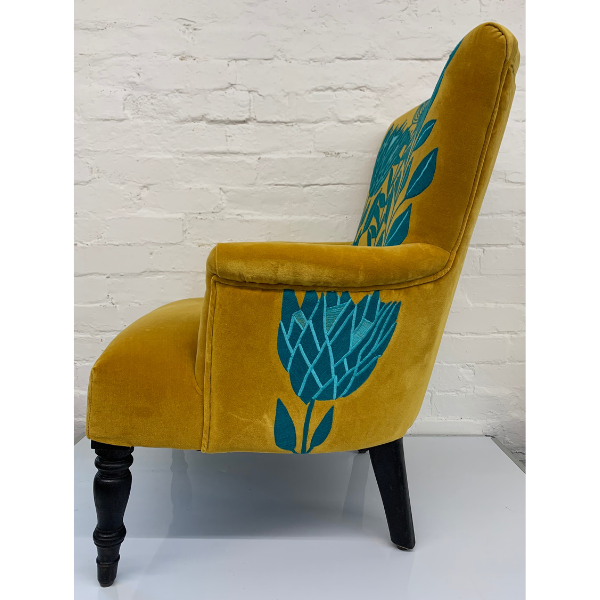 Image of back side of a velvet mustard arm chair with turquoise waratah embroidered.