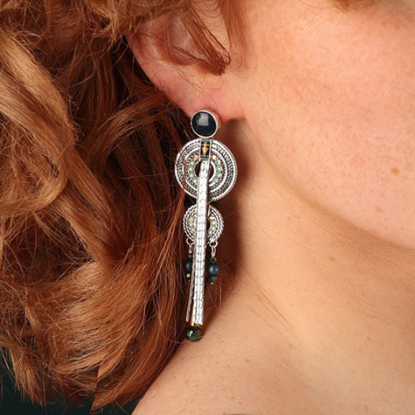 Image of model wearing tribal style silver disc earrings embellished with gold, blue and turquoise beads, a hand painted motif and silver tassels.