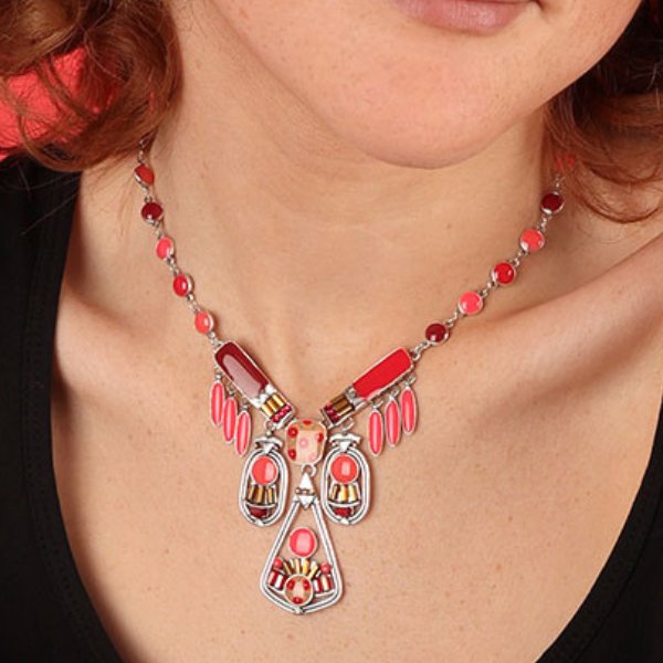 Image of model wearing statement necklace with multiple hand painted motifs in many shades of pink on silver metal finish.