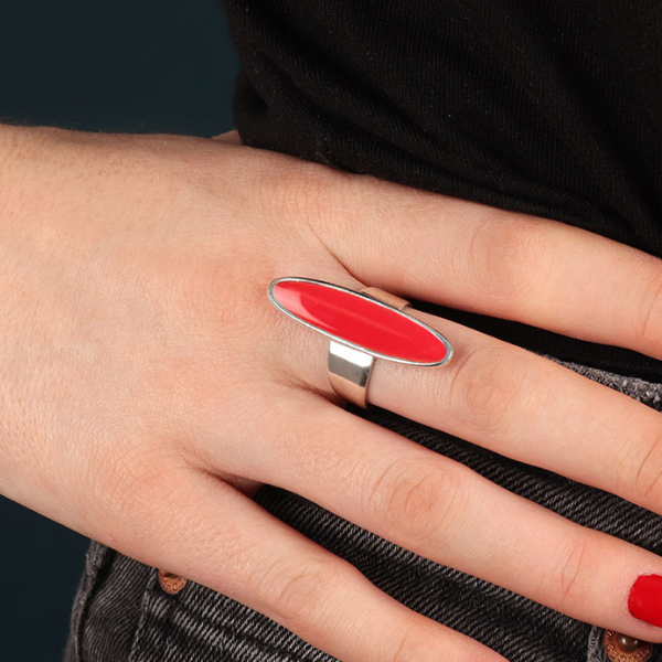 Image of model wearing elongated oval shape ring enamelled in red on silver plated adjustable band.