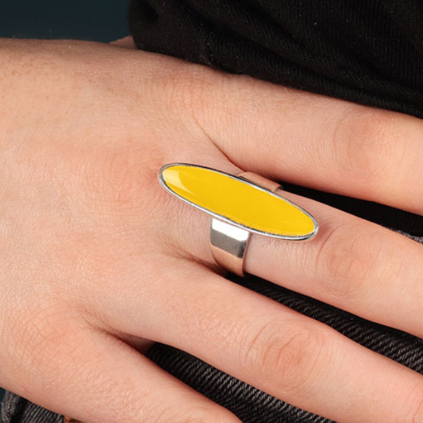 Image of model wearing elongated oval shape ring enamelled in yellow on silver plated adjustable band.
