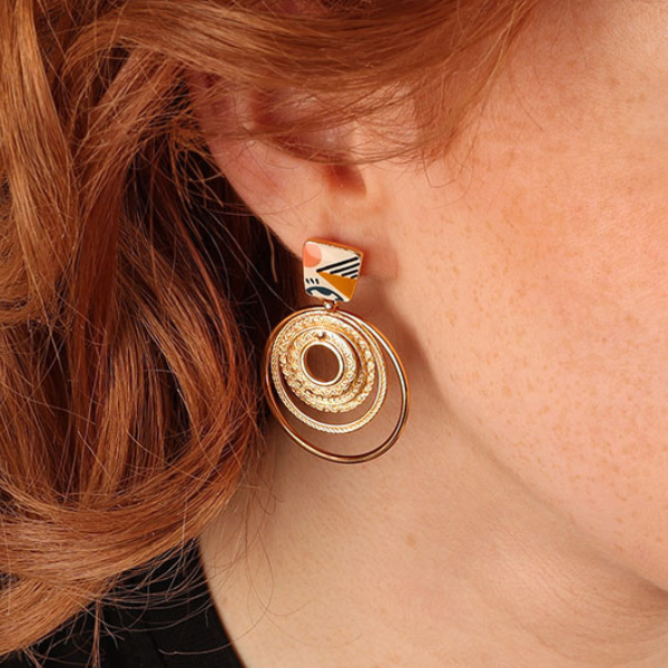 Image of model wearing quirky multicoloured motif earrings with 3 ring dangles on french hook gold metal finish.