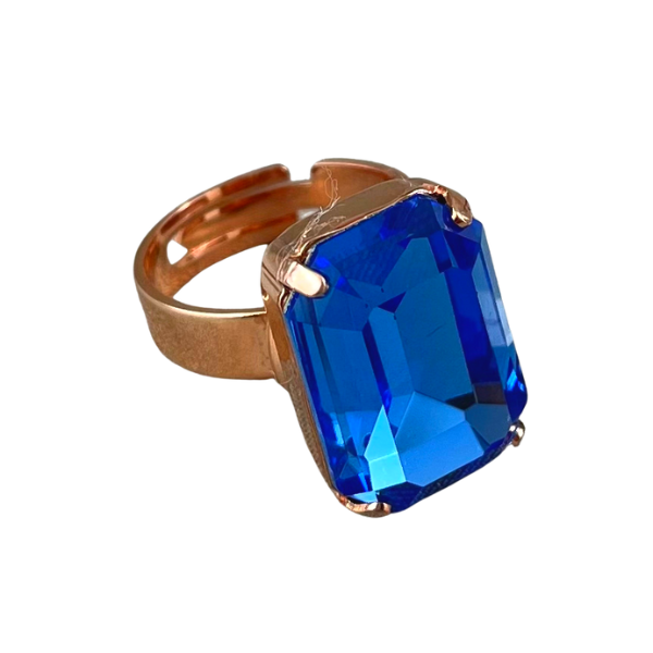 Image of dress ring featuring a large, rectangular blue crystal on an adjustable 18ct rose gold plated band.