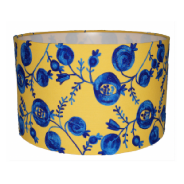 Pomegranate Pomp Drum Lampshade features a vibrant cobalt blue pomegranate design that overlays a sunny yellow cotton/linen blend background.