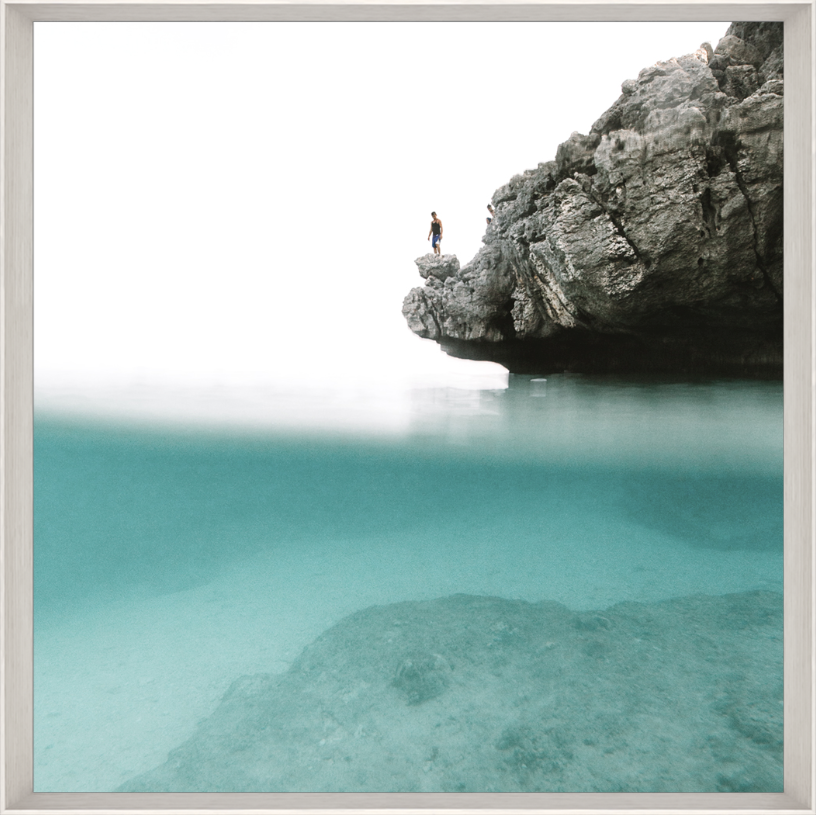 Man standing on edge of rock with blue water below