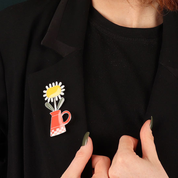 Image of model wearing bright pretty brooch with yellow and white sunflower sitting in a red watering can all on silver metal pin finish.