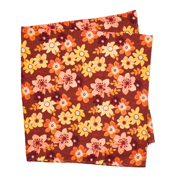 Image of linen tablecloth with yellow, peach and ochre flowers on a rust brown background.