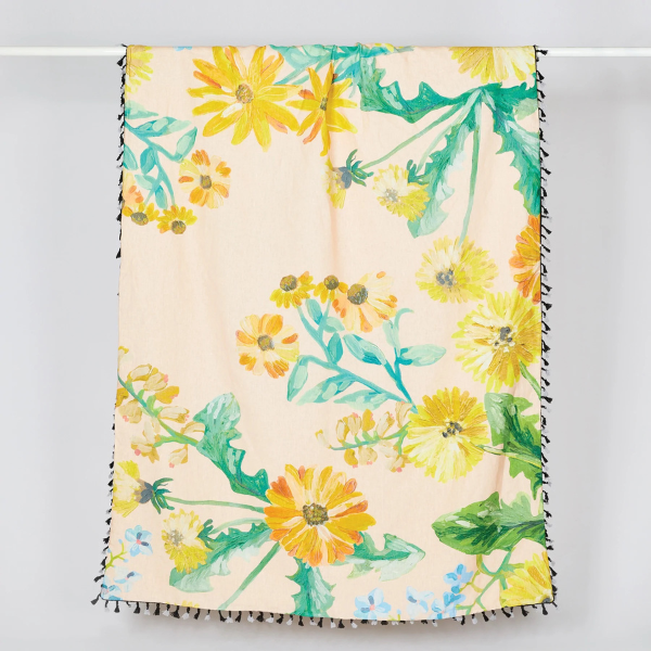 Image of linen throw with original dandelion print. Yellow flowers on peach background. Black and grey tassel edging.