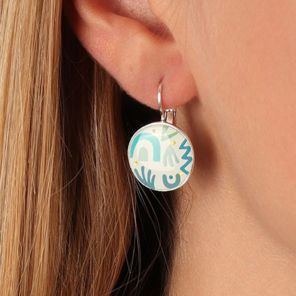 Image of model wearing dainty round earrings with hand painted white with blue patterns.